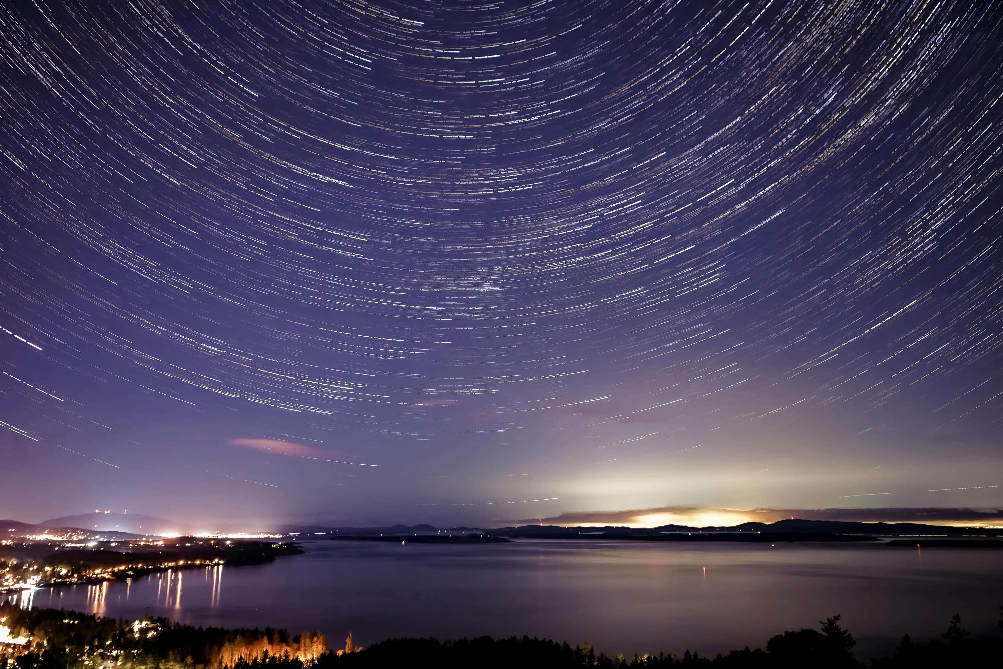 Glowing Lights Of City On Seashore Under Starry Sky